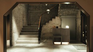 Un escalier avec une rampe en bois menant à un palier où se trouvent une porte et un petit meuble en bois.