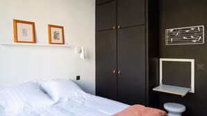 A bedroom with a bed, a wardrobe, a toilet, and two framed pictures on the wall. - APARTMENT WITH MAGNIFICENT VIEW OF THE OLD PORT (Marseille)