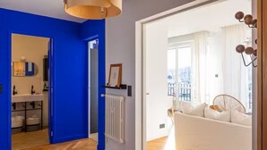 A room with a blue wall, a white radiator, a white sofa, and a window with a view of buildings. - APARTMENT WITH MAGNIFICENT VIEW OF THE OLD PORT (Marseille)