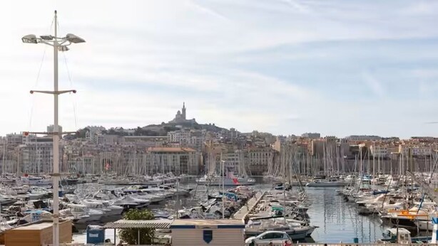 A marina with numerous boats docked, a prominent building with a tower in the background, and a clear sky. - APARTMENT WITH MAGNIFICENT VIEW OF THE OLD PORT (Marseille)