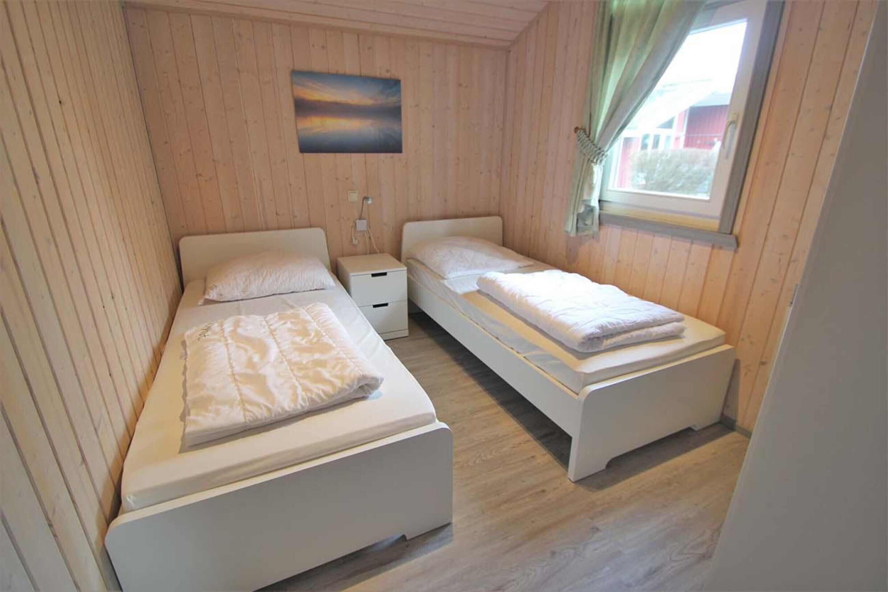 Een knus kamertje met twee bedden, een nachtkastje en een raam met gordijnen.