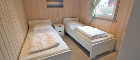Une petite chambre agréable, dotée de deux lits, d’une table de chevet et d’une fenêtre avec des rideaux.