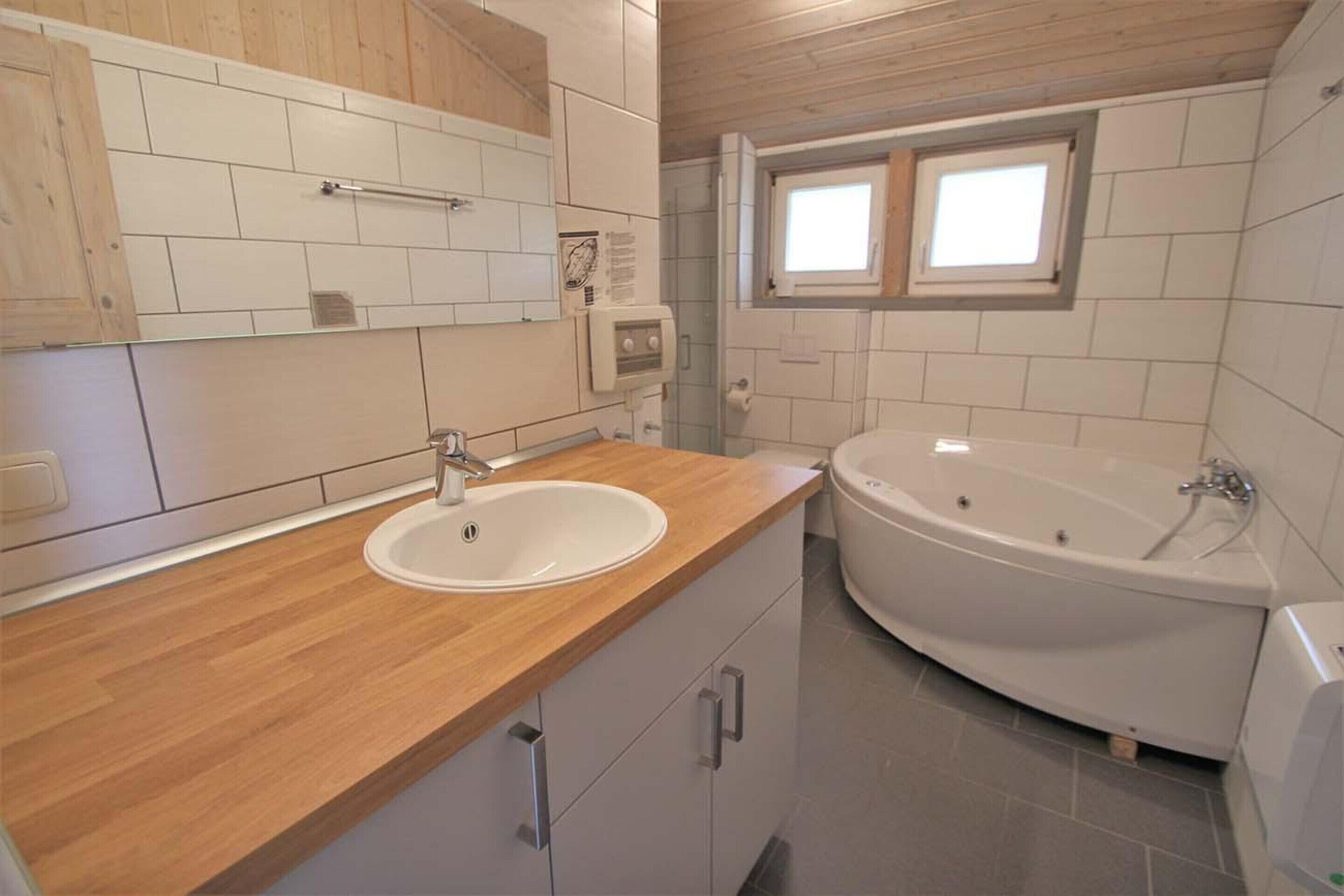 Une salle de bain avec un meuble-lavabo en bois, un lavabo blanc, une baignoire sur pieds et une fenêtre située au-dessus de la baignoire.