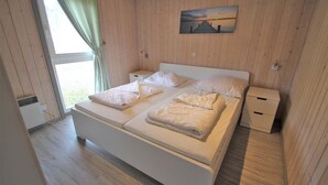 Een slaapkamer met een groot bed, twee nachtkastjes, een raam met gordijnen en een schilderij aan de muur.