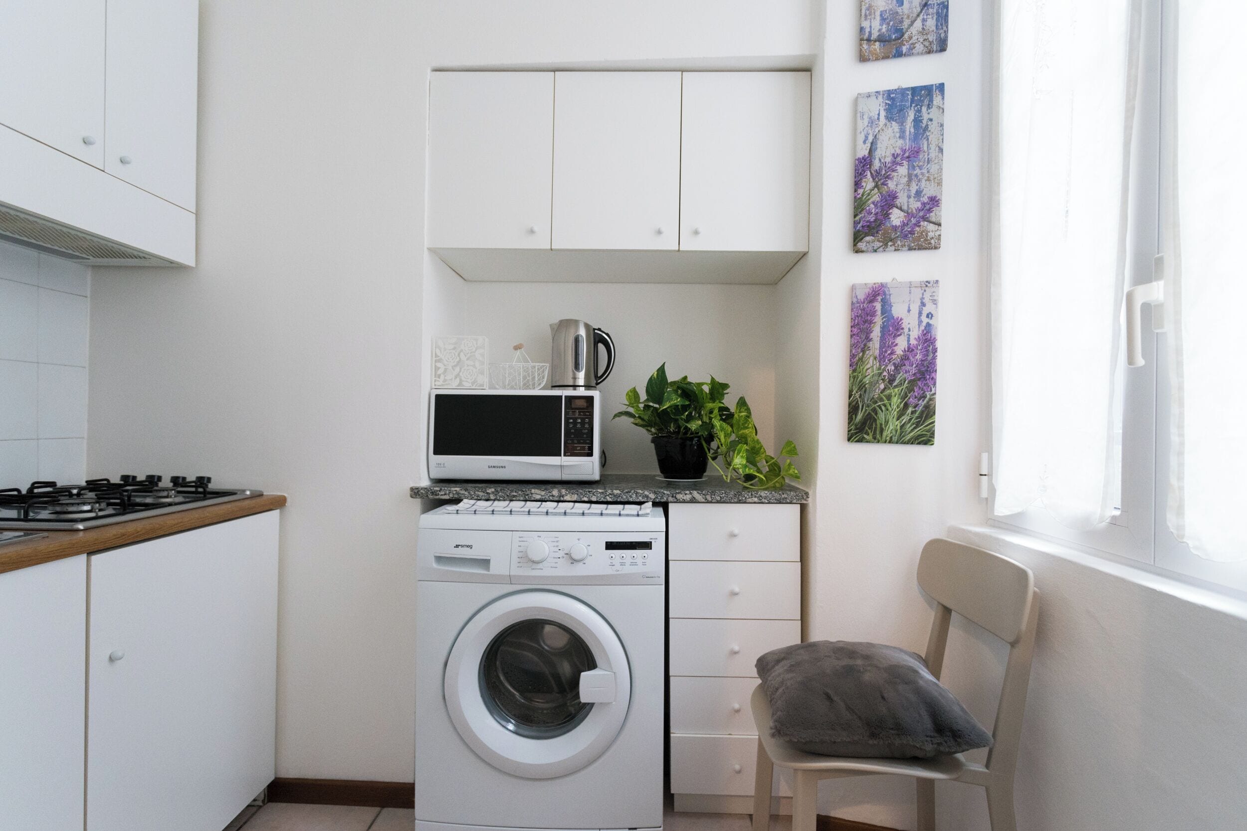 Cozinha compacta com máquina de lavar, micro-ondas e uma pequena área de refeições, com cadeira e mesa.