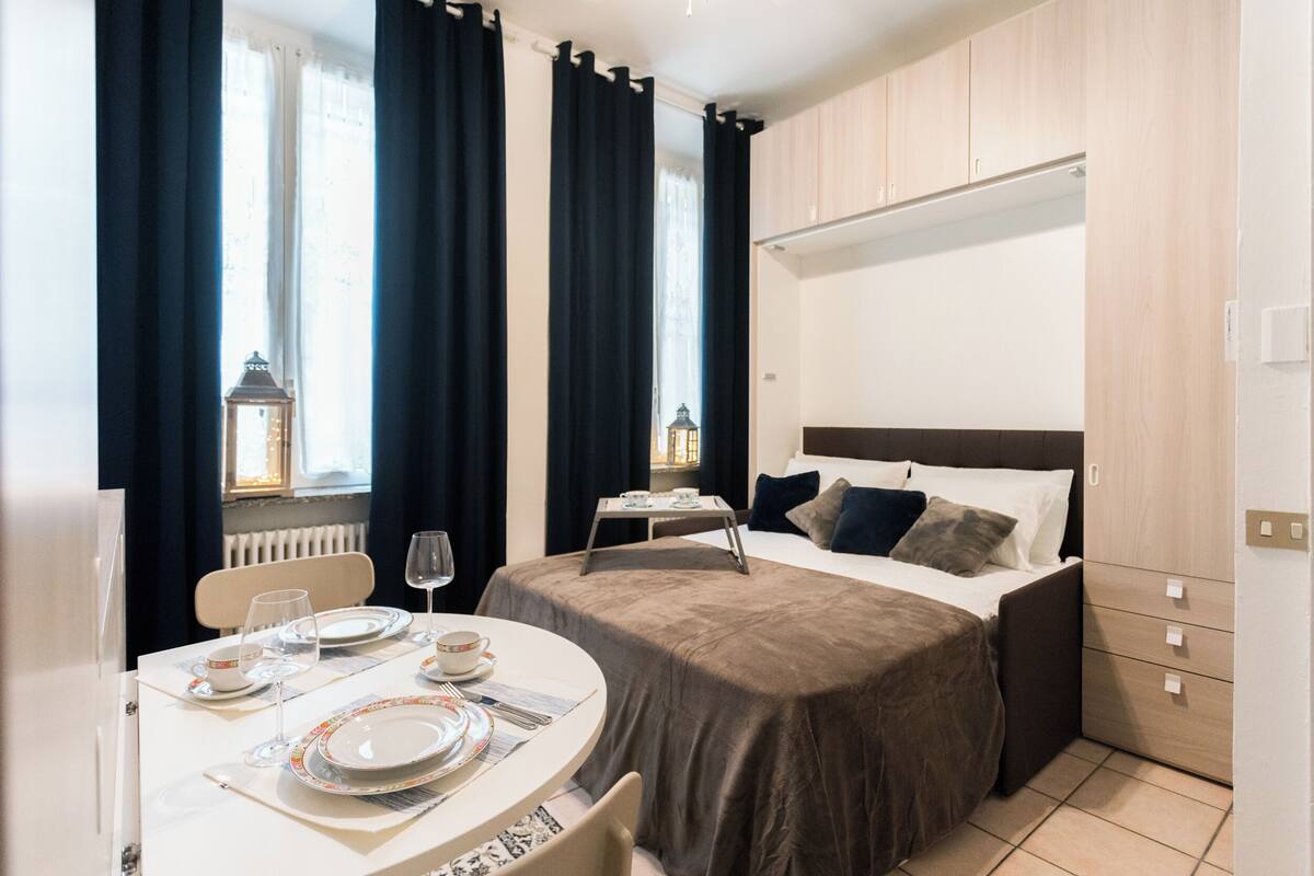 Ein Hotelzimmer mit einem Bett, einem für das Frühstück gedeckten Tisch und einem mit Vorhängen versehenen Fenster.
