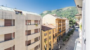 Un edificio de varios pisos con balcones, una calle arbolada y una montaña al fondo.