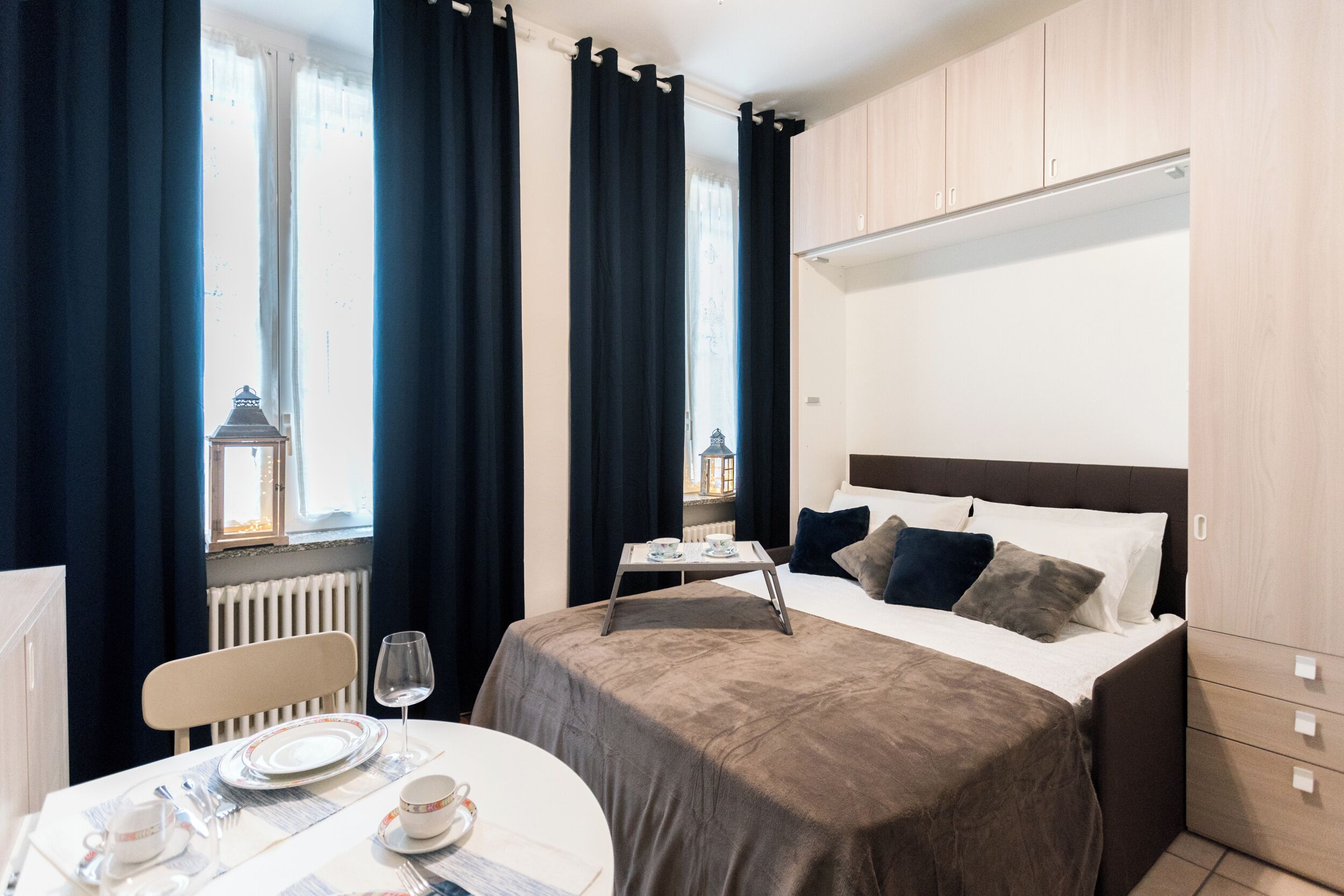 A hotel room with a bed, bedside table, and a view of a building through the window.