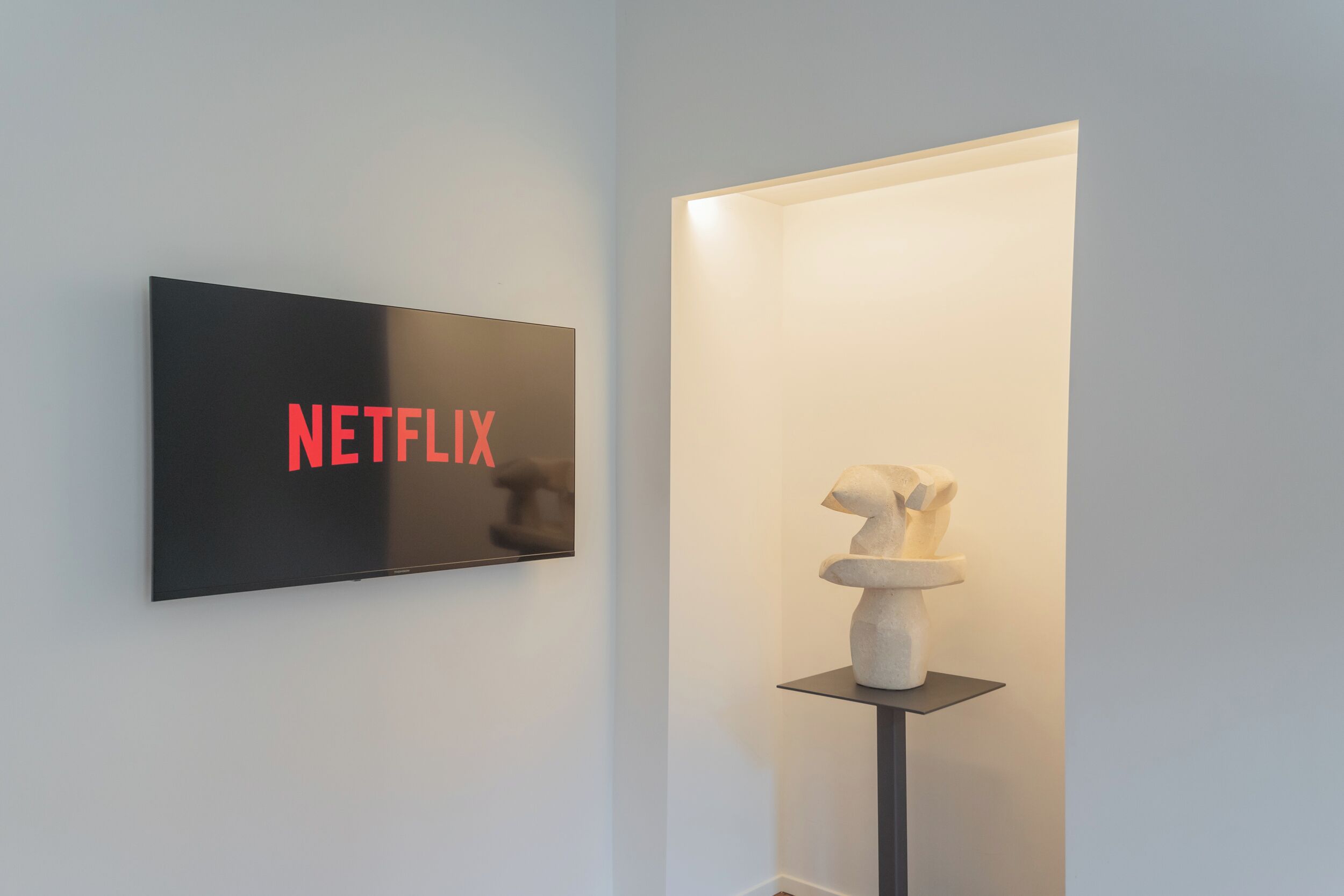 A wall-mounted sign with the word "NETFLIX" in red letters, a sculpture on a pedestal, and a door with a light source.