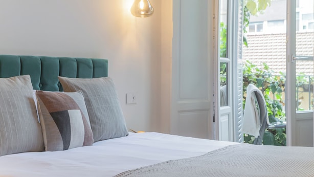 A bedroom with a bed, pillows, a hanging light fixture, and a view of greenery outside. - Como Liberty Suites - Garbo by Rent all Como (Como)