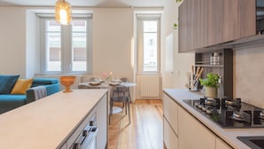 A modern kitchen with a central island, wooden cabinets, and a dining area with a table and chairs. - Como Liberty Suites - Garbo by Rent all Como (Como)