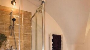 Una ducha con cerramiento de vidrio, suelo de baldosas, un perchero y una vela decorativa.