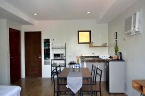 A compact kitchen with a dining table, chairs, a microwave, a sink, and a refrigerator. - MCA Suites by Hiverooms (Cebu City)