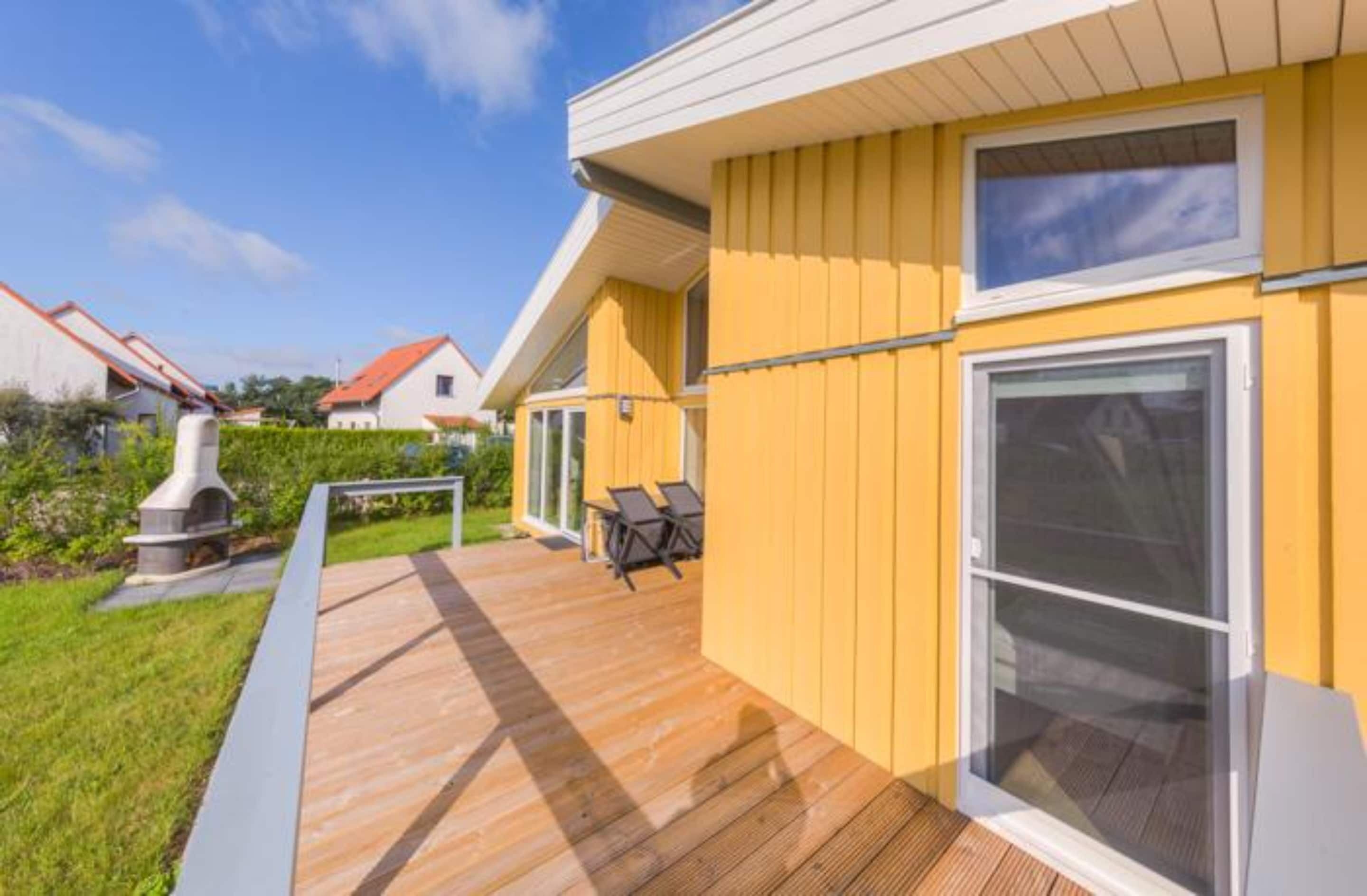 Un bâtiment jaune doté d’une terrasse, d’un barbecue et d’une porte-fenêtre coulissante.