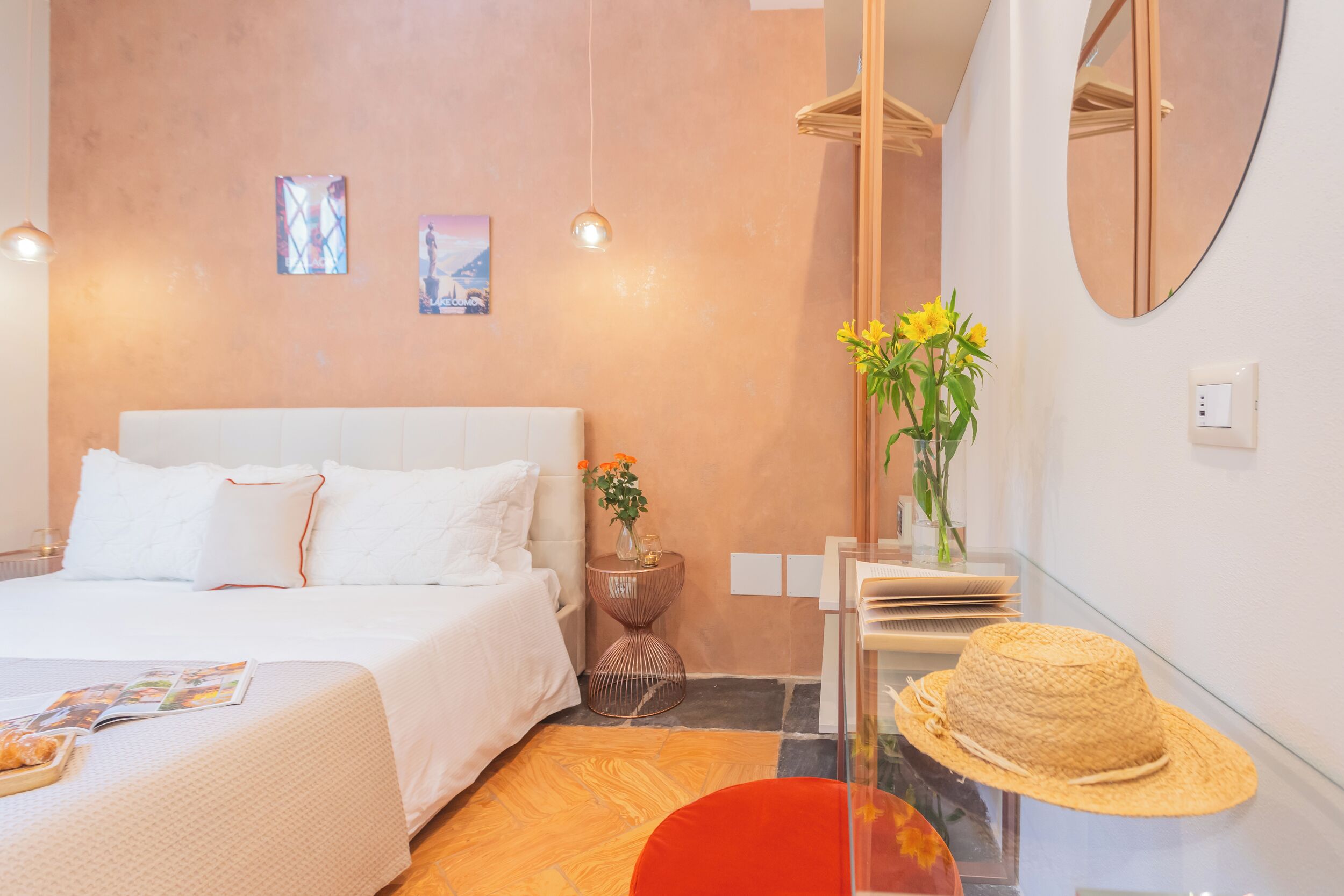 A hotel room with a bed, a bedside table with a vase of flowers, a mirror, and a red chair.
