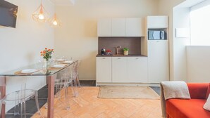 Ett modernt kök med vita skåp, en matplats med genomskinliga stolar och ett glasbord, och en röd soffa i vardagsrummet.