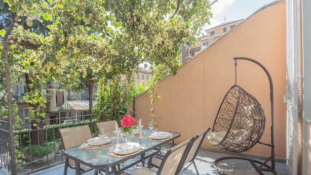 A dining area with a round table set for four, surrounded by chairs, a hanging chair, and a potted plant with flowers. - Como Liberty Suites - Gatsby by Rent all Como (Como)