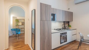 A modern kitchen with a built-in oven, a sink, and a microwave. There is a blue chair and a dining table in the adjacent dining area. - Como Liberty Suites - Gatsby by Rent all Como (Como)