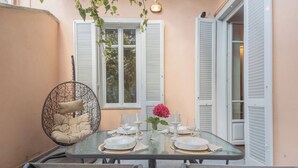 A dining area with a glass table set for six, surrounded by chairs, a hanging chair, and a window with shutters. - Como Liberty Suites - Gatsby by Rent all Como (Como)