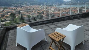 A terrace with two white chairs and a small wooden table, overlooking a cityscape with mountains in the background. - Como Panorama by Rent all Como (Como)