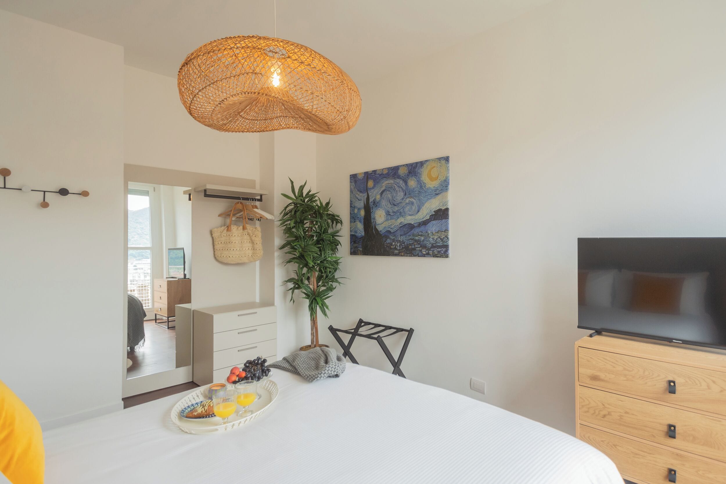 Une chambre moderne avec un grand lit, une télévision, une lampe en osier, un tableau et un plateau de petit-déjeuner.
