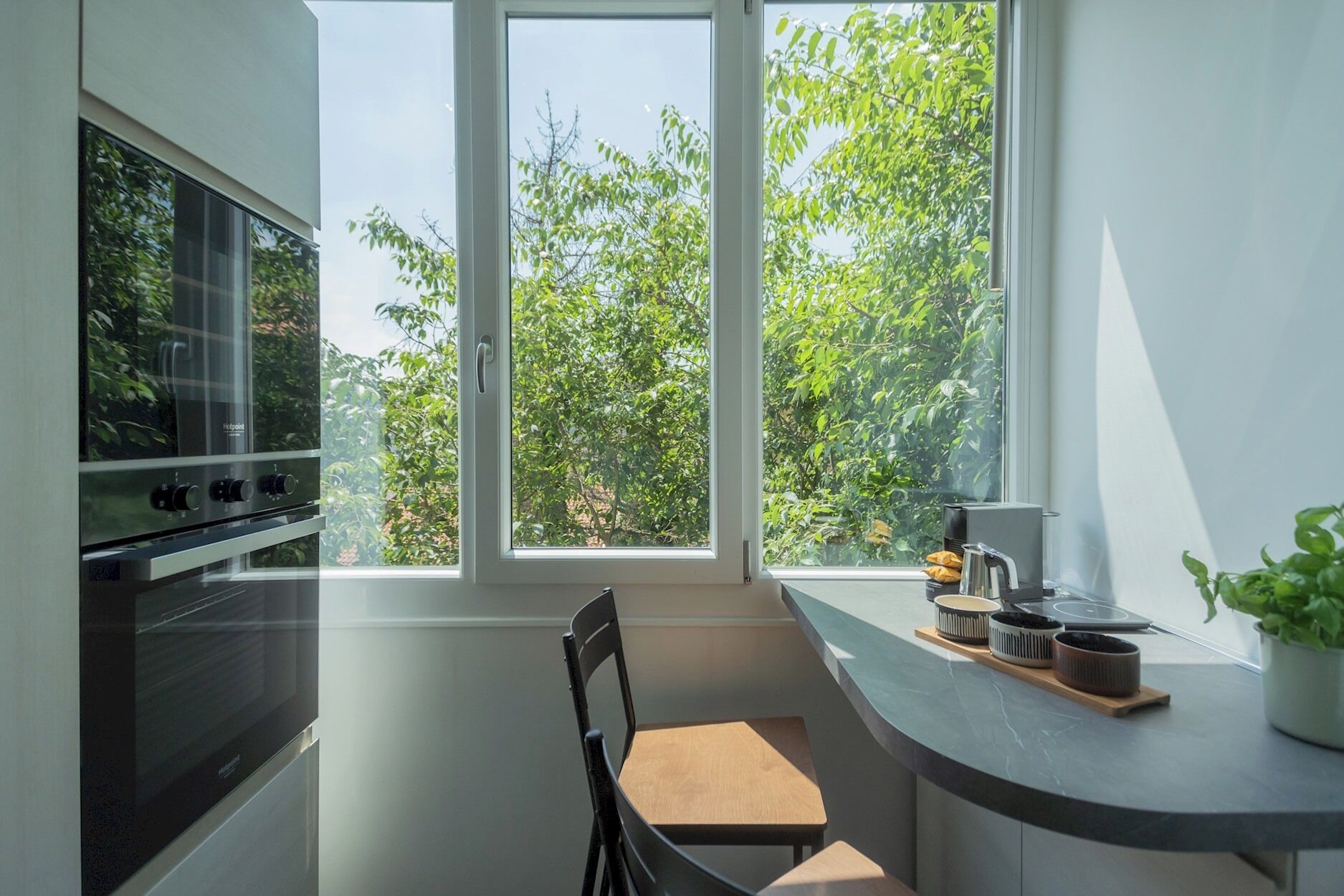 Une cuisine moderne avec une grande fenêtre, un four encastré et une chaise en bois.