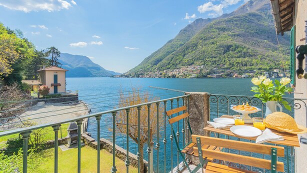 A terrace with a table set for breakfast overlooking a lake and mountains. - Deriva Apartment on Careno's Beach by Rent all Como (Nesso)