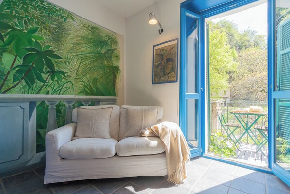 Un sofá blanco con una manta beige, un mural grande con motivos vegetales y un cuadro abstracto enmarcado en la pared.