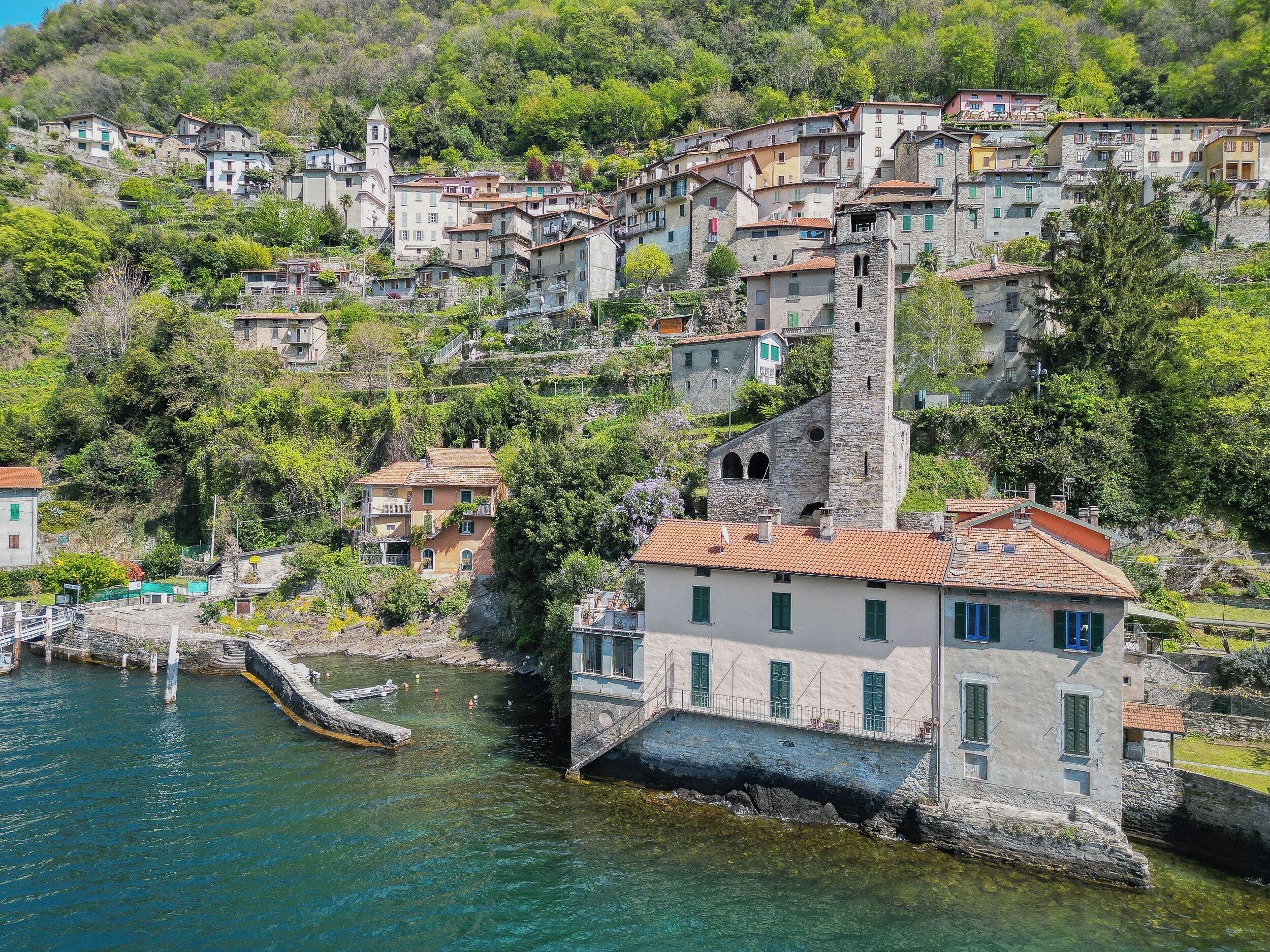 A coastal village with stone buildings, a prominent tower, and a clear view of the sea.