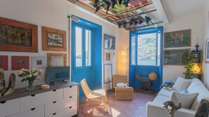 A cozy living room with a white sofa, a wicker chair, a TV, and artwork on the walls. - Deriva Apartment on Careno's Beach by Rent all Como (Nesso)