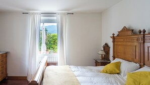 Een slaapkamer met een houten bed, witte beddengoed en uitzicht op groen.