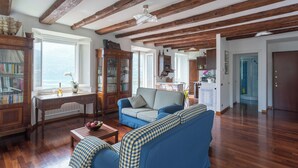 Een ruime woonkamer met houten balken, een blauwe bank, een houten salontafel en een boekenkast.