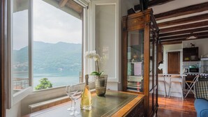 Een kamer met uitzicht op bergen en een meer, een houten tafel met een fles en een glas, en een blauwe bank.