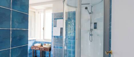 A bathroom with blue tiles, a glass shower enclosure, a vanity with a mirror, and a window providing natural light.