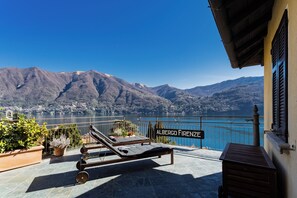 Una terraza con dos tumbonas, un letrero que dice "Albergo Firenze" y vistas a montañas y un lago.