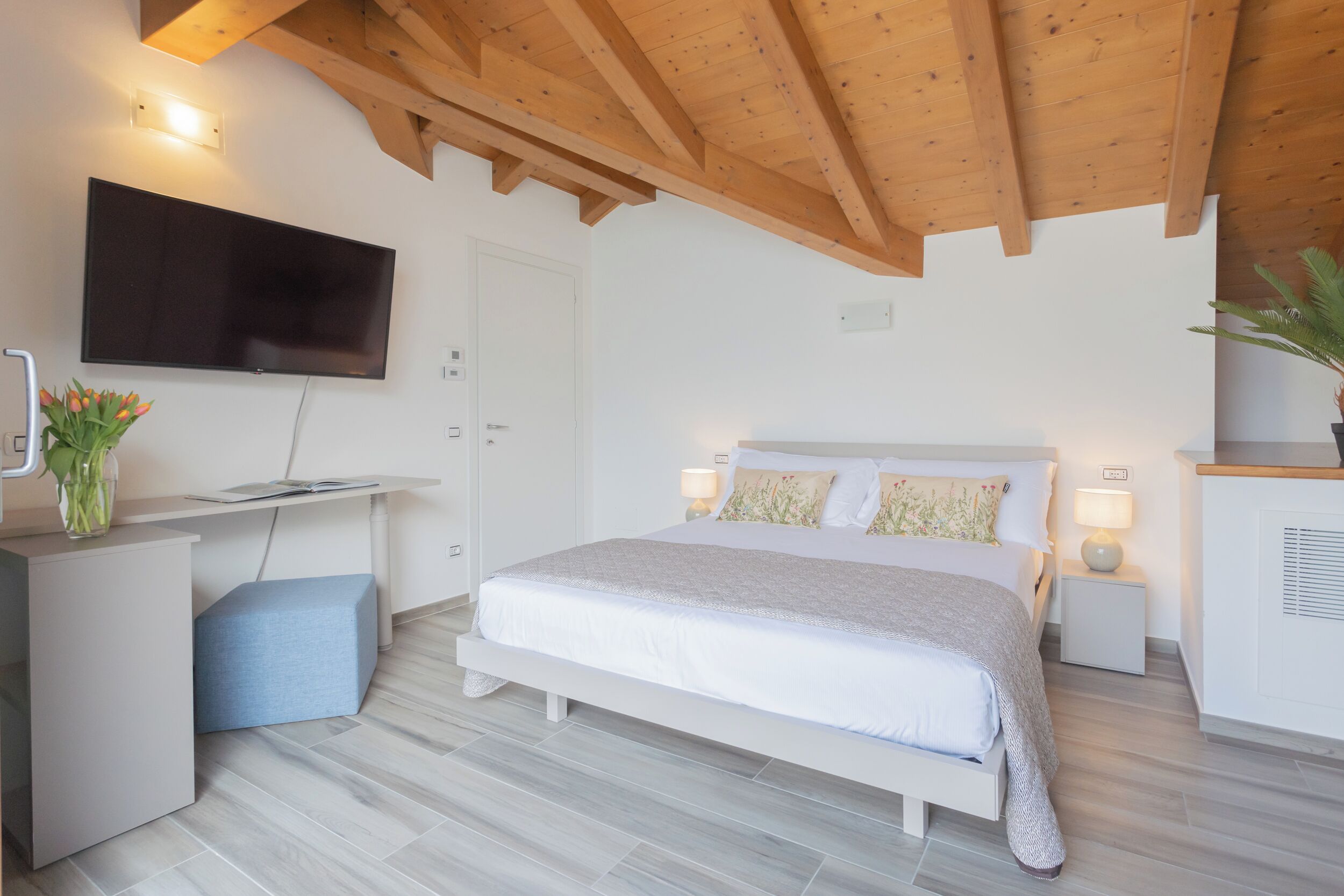 Ein Schlafzimmer mit einem Bett, Nachttischen, einem Fernseher und einem Schreibtisch mit einer Pflanze.