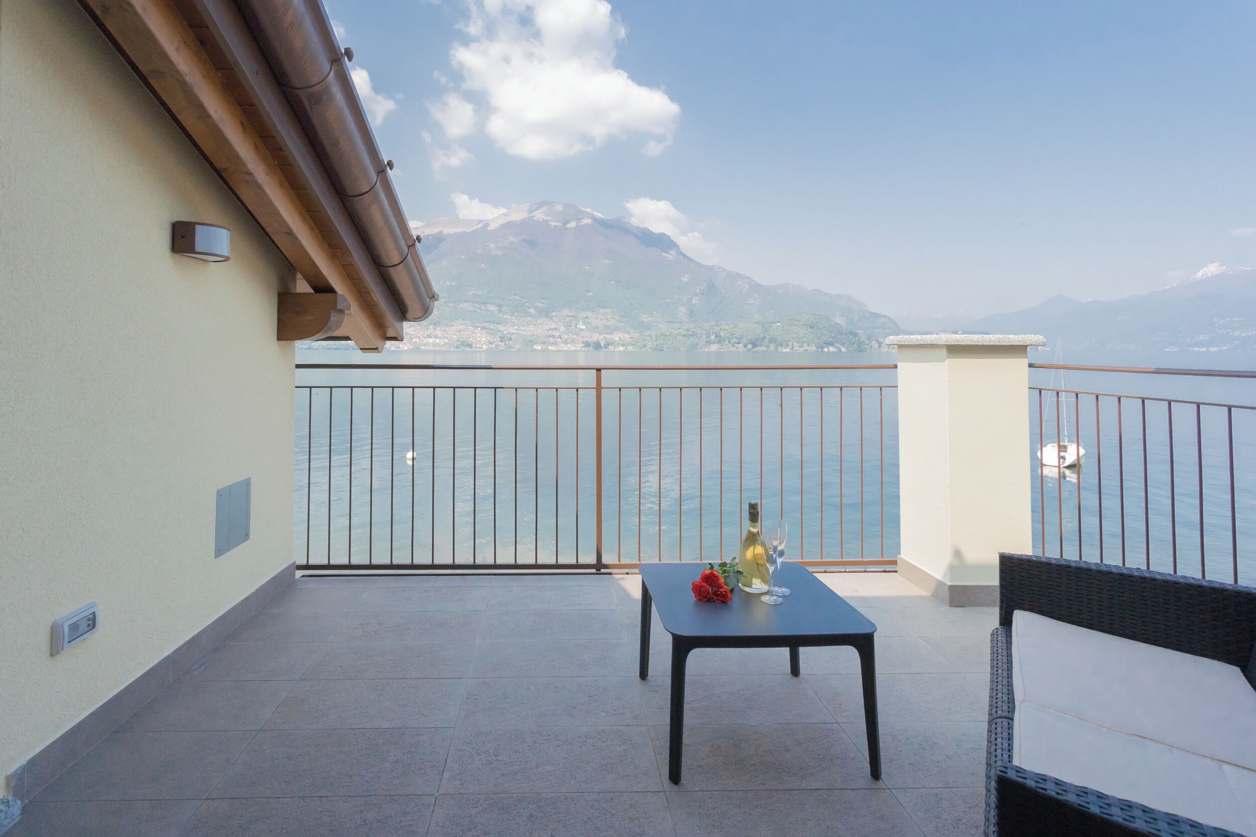 A balcony with a table, a bottle of wine, and a chair. A mountain is visible in the background.