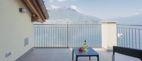 A balcony with a table, a bottle of wine, and a chair. A mountain is visible in the background.