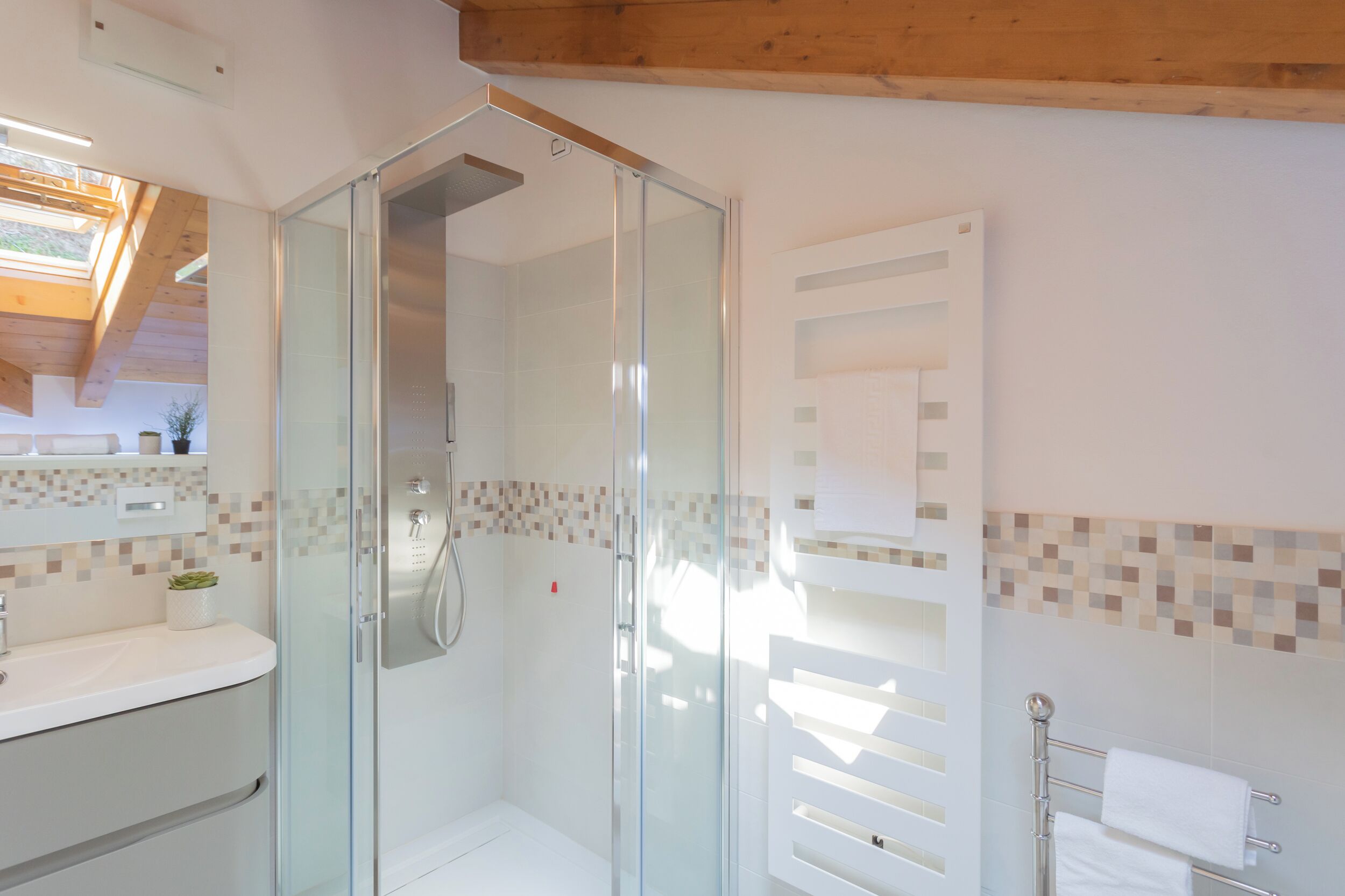 A modern bathroom with a glass shower enclosure, a white sink, and a tiled backsplash.
