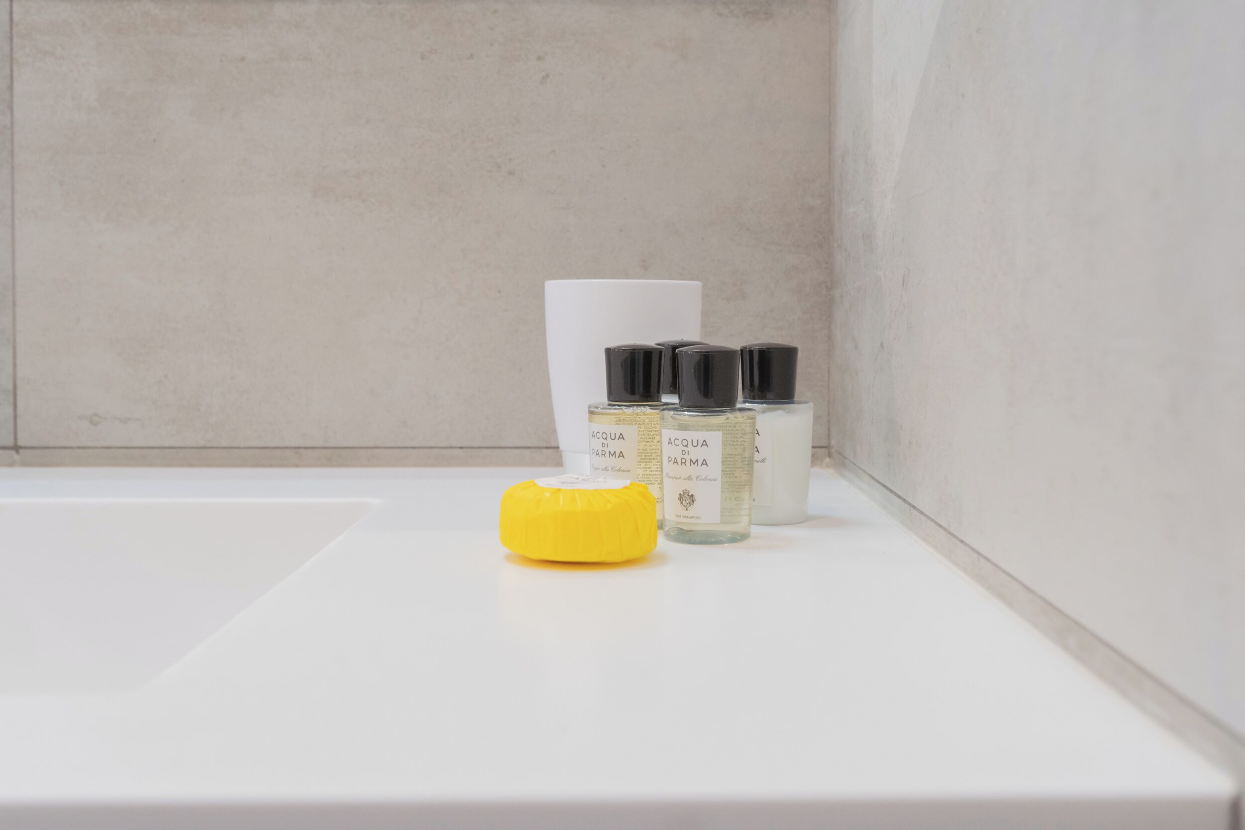 A bathroom with a white sink, a yellow soap dispenser, and two bottles of Acqua di Parma cologne.