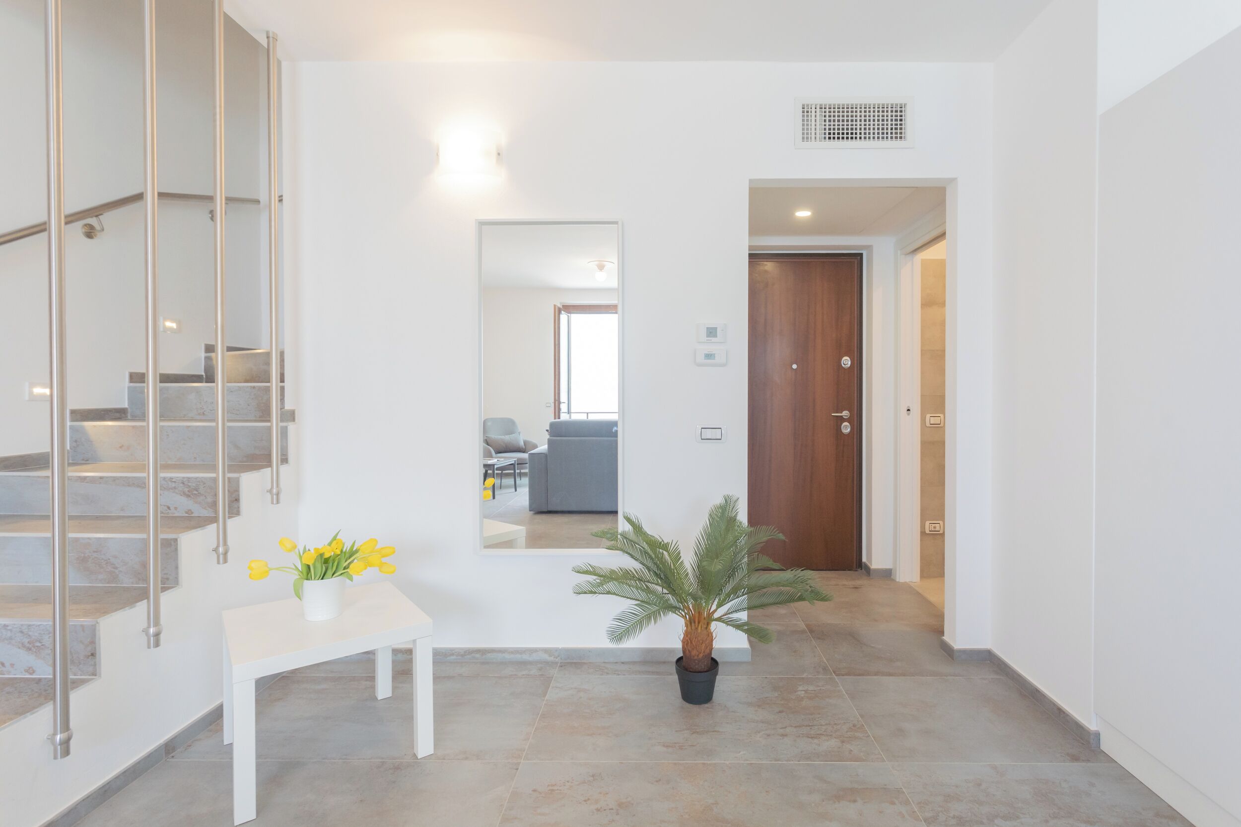Un interior moderno con una escalera, un banco blanco con una planta en maceta y una puerta que da a otra habitación.