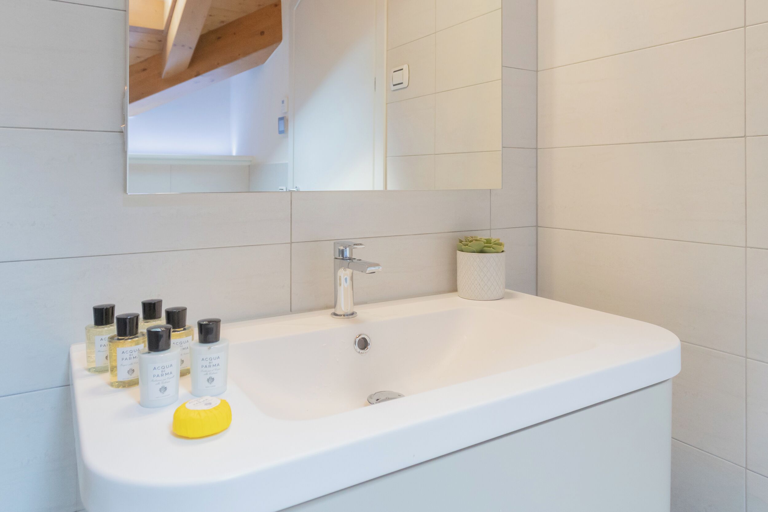 A white bathroom with a large sink, a mirror, and several bottles of Acqua Parma.