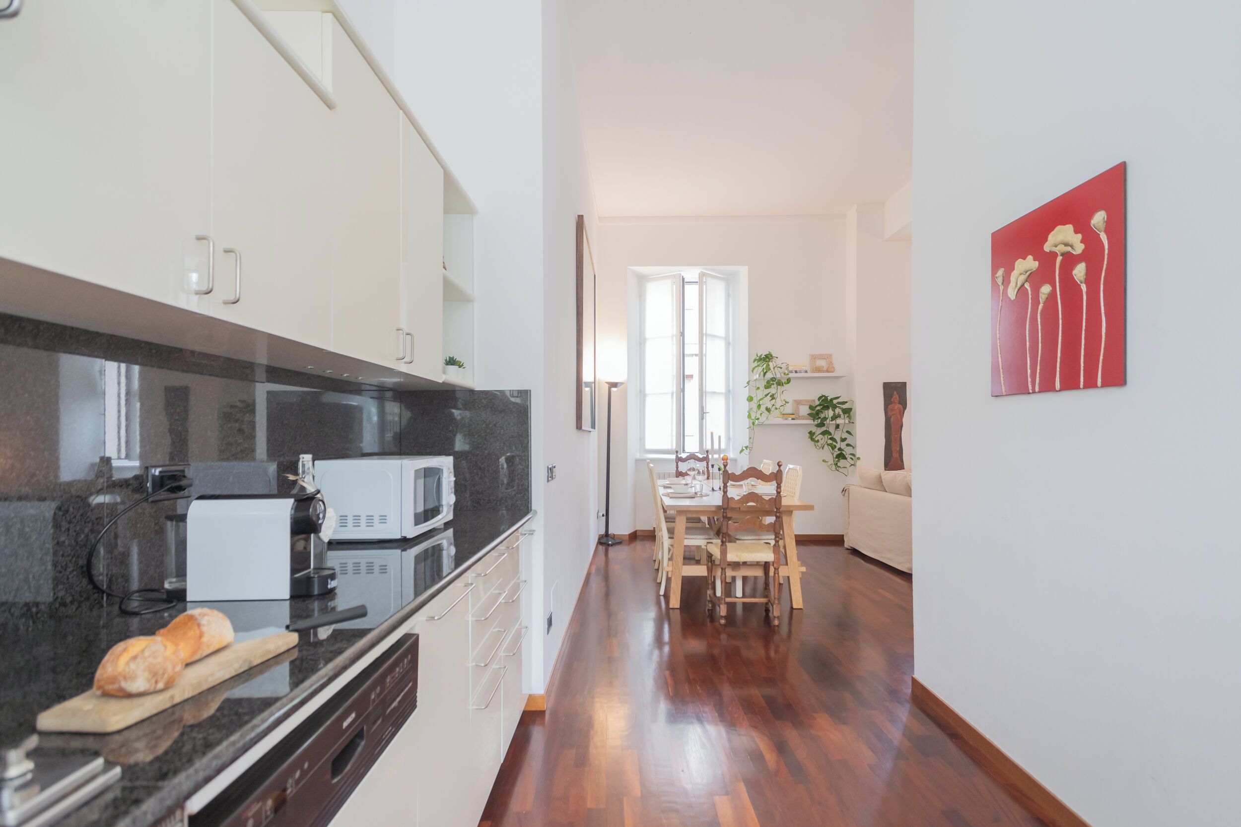 Una cocina moderna con encimera negra, armarios blancos y un comedor con mesa y sillas de madera.