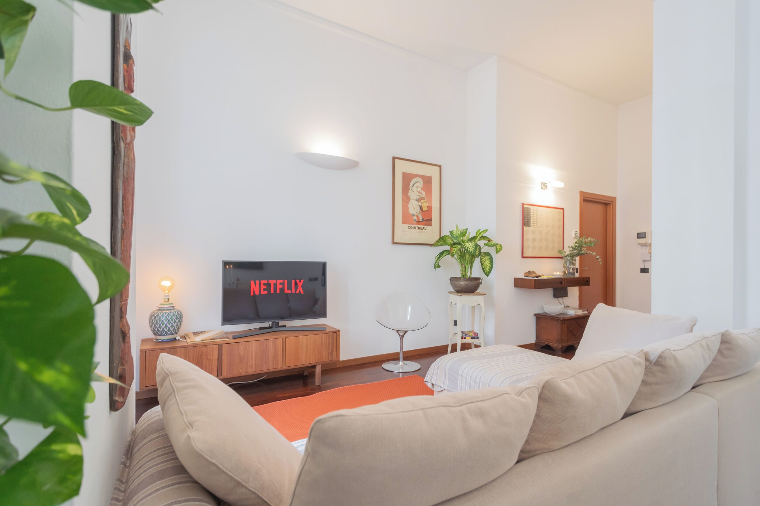 Un salon avec un téléviseur affichant le logo « NETFLIX », un canapé, une table basse, une plante en pot et un tableau encadré au mur.