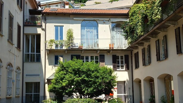 A courtyard with cobblestone pavement, surrounded by buildings with balconies and windows, and a tree in the center. - Filanda - Best Lakefront in Como by Rent all Como (Como)