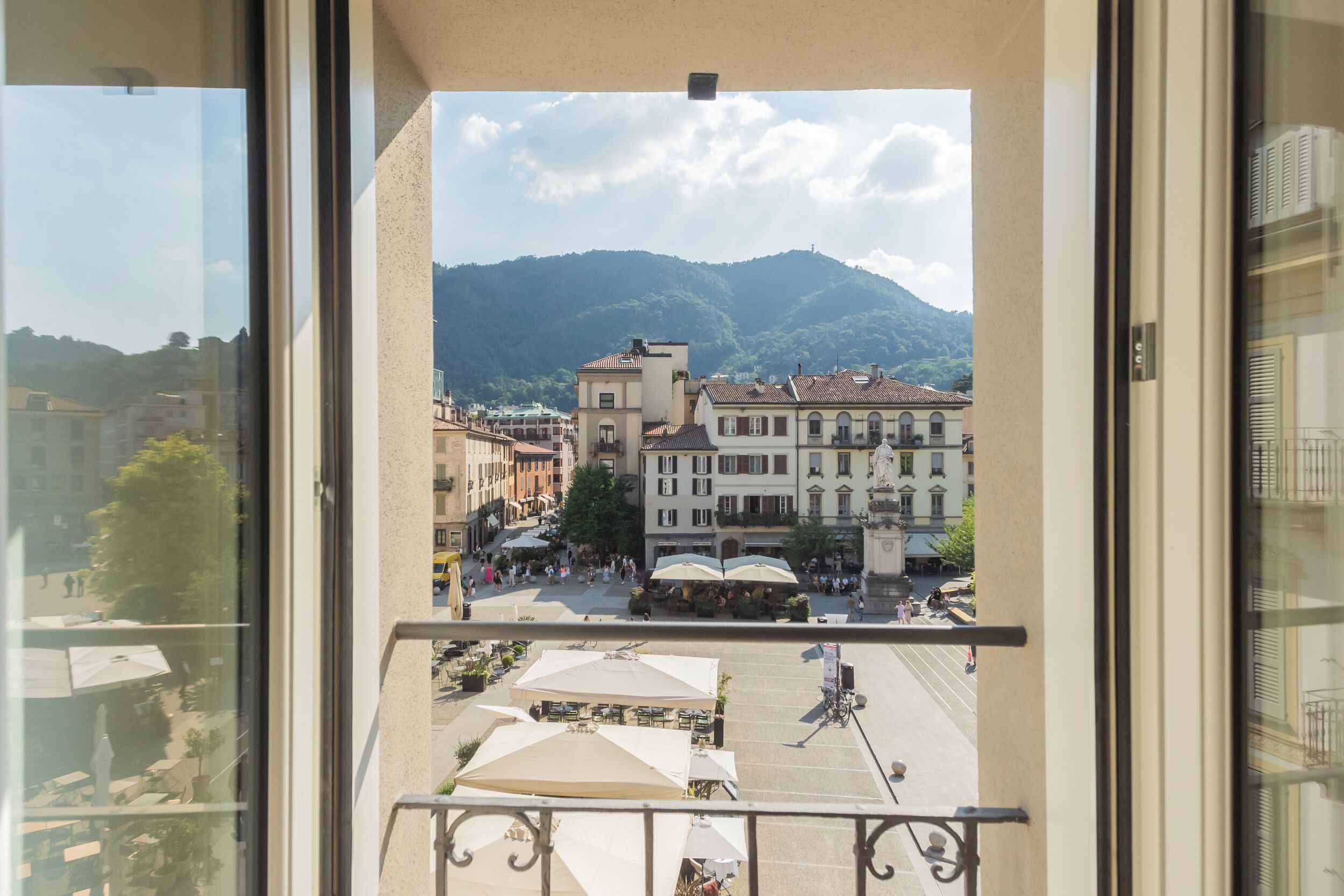 A balcony with a view of a town square, buildings, and mountains.