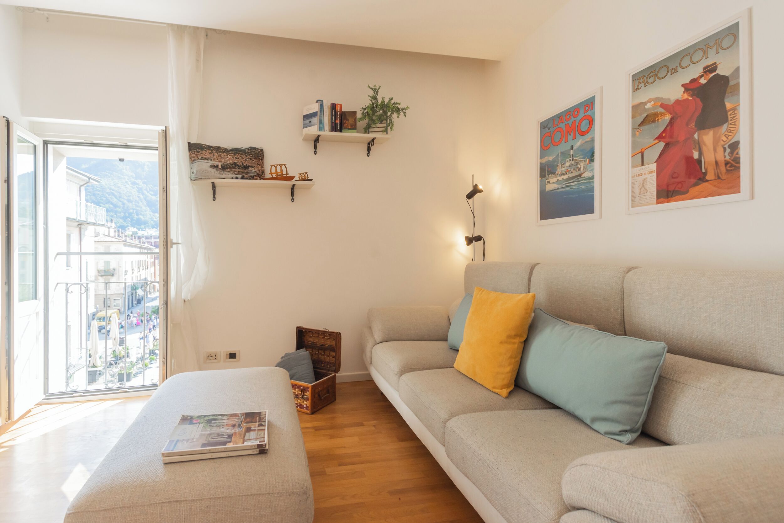 Ein Wohnzimmer mit einer Couch, einem Couchtisch und Blick durch eine Glastür. An zwei Wandregalen befinden sich Bücher und eine Pflanze.