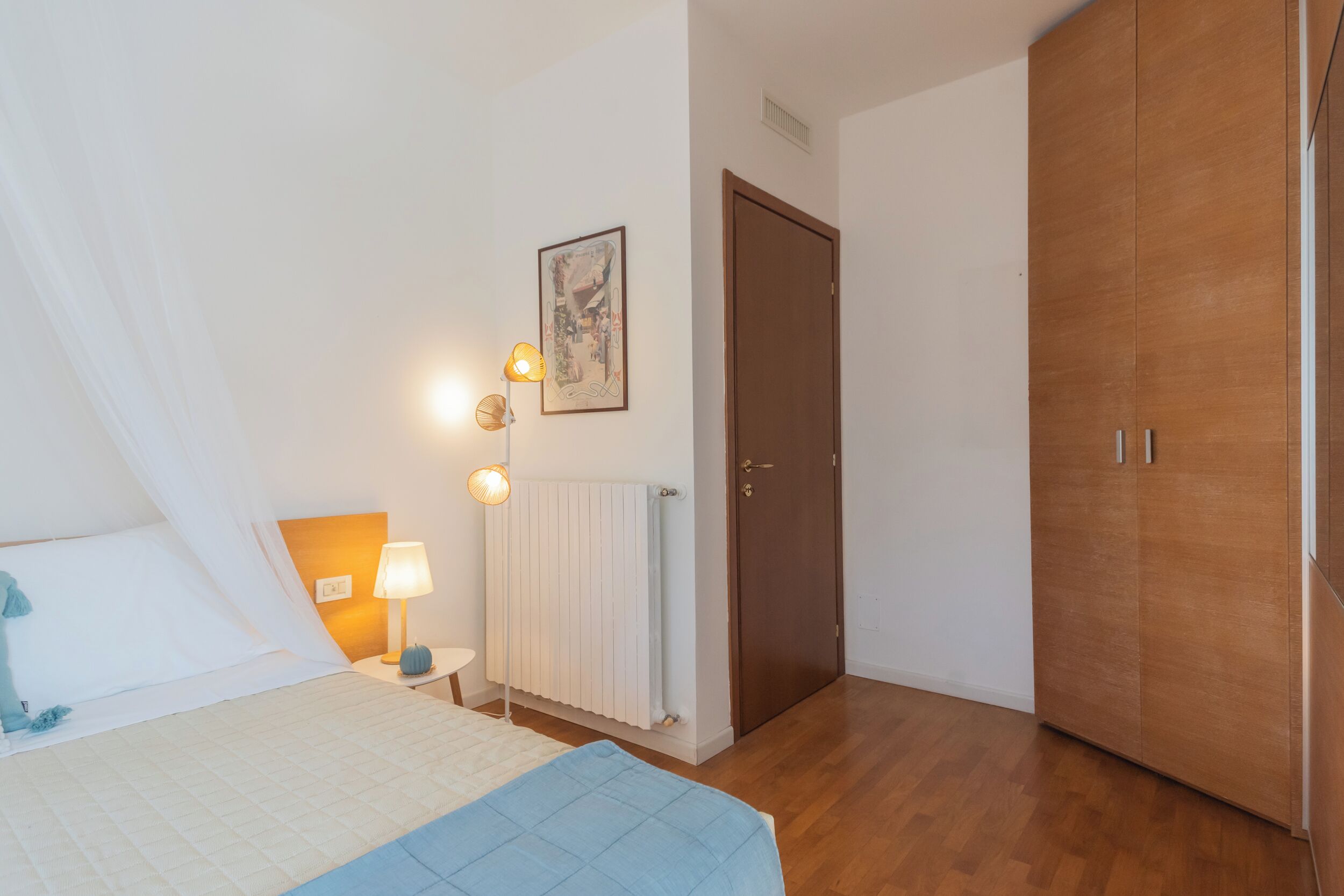 A bedroom with a bed, bedside lamps, a radiator, a door, and a wardrobe.