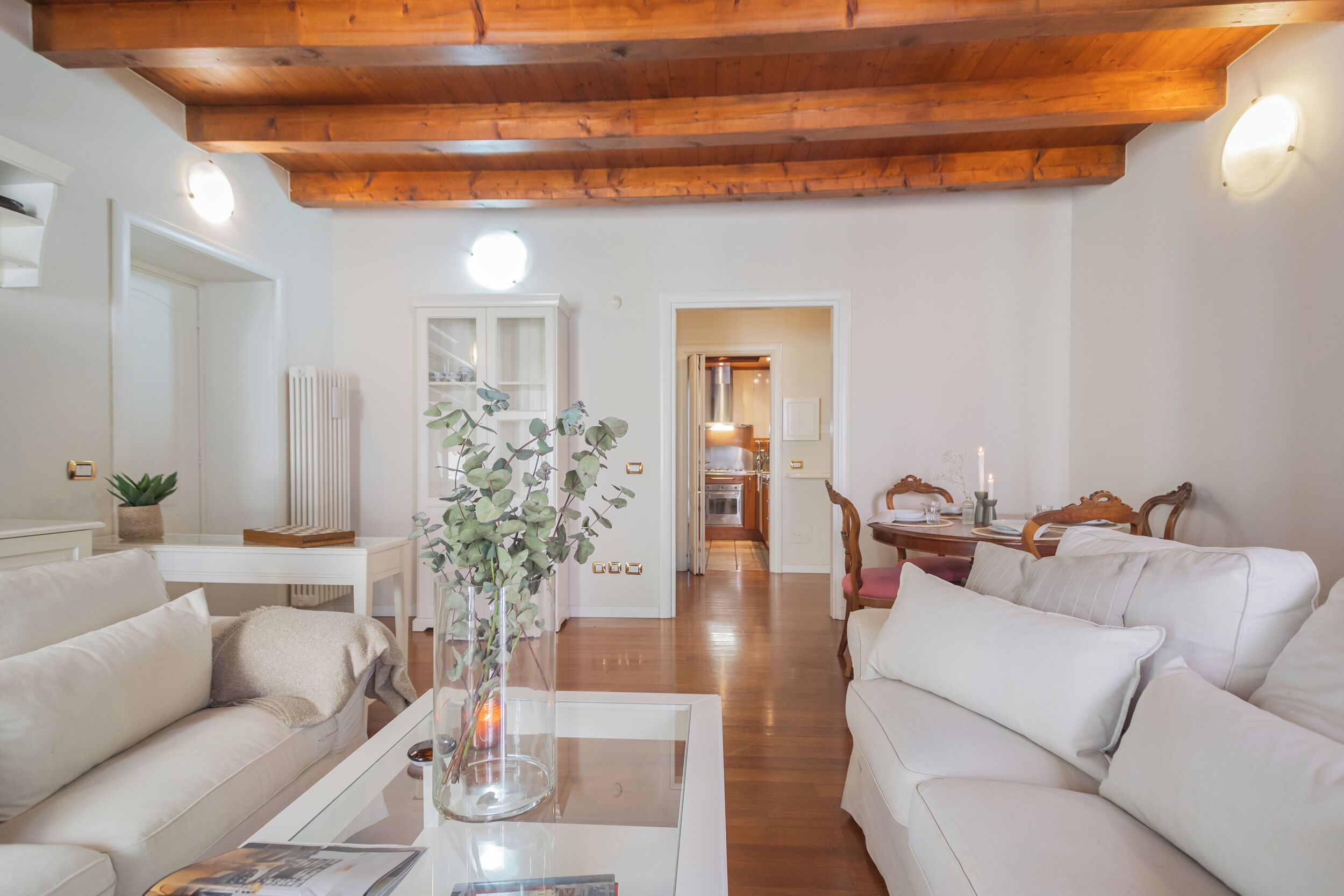 A living room with a white sofa, a coffee table with a vase, and a wooden ceiling.