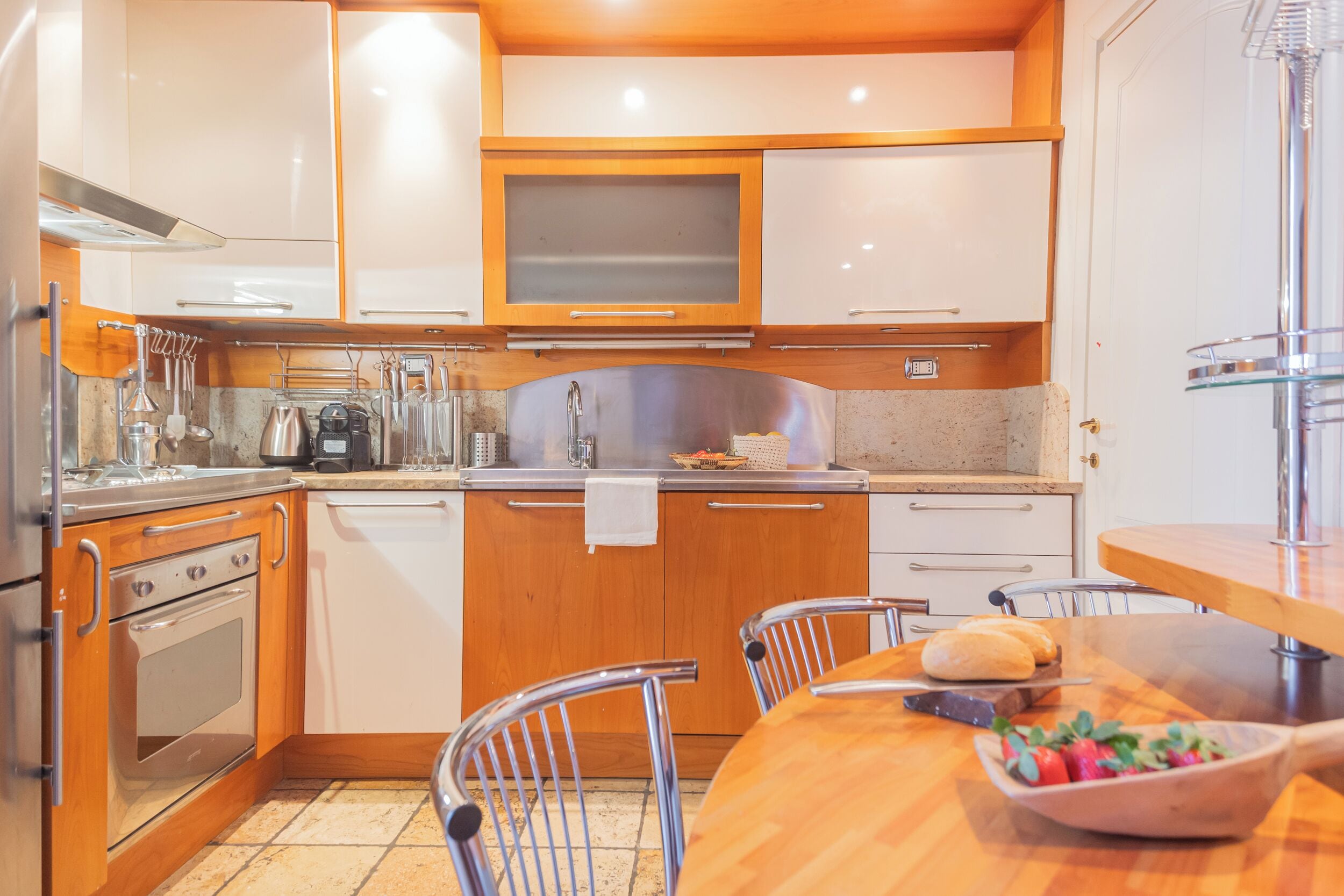 Een compacte keuken met houten kastjes, roestvrijstalen apparatuur en een eethoek met een houten tafel en stoelen.